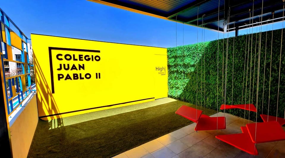 Muro gráfico institucional y módulos de asiento rojos suspendidos en terraza techada